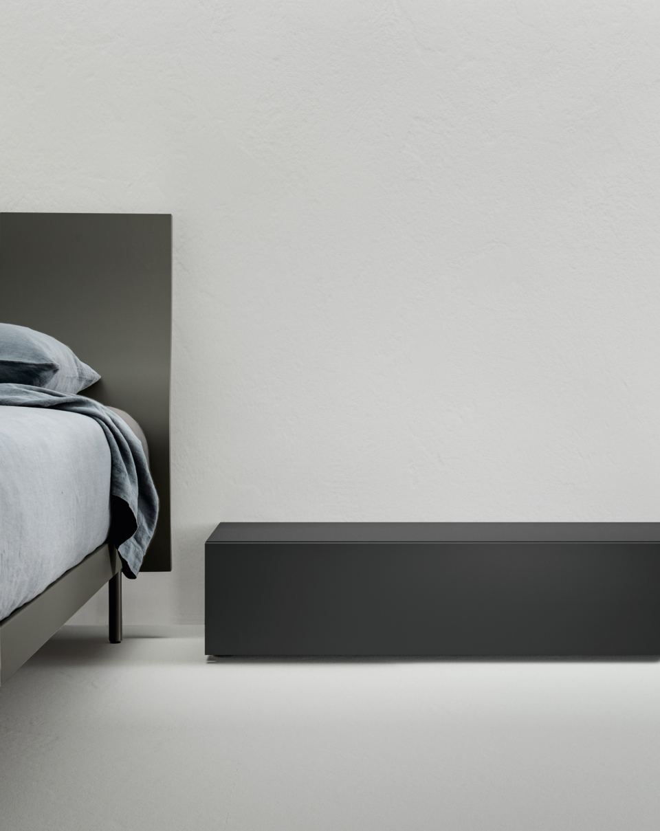 A clear horizontal line picks up the silhouette of the bed and slews it over the adjoining wall, creating a modern, striking geometry. 
The drawer is equipped with a soft-closing mechanism for an even more pleasant experience. 
The Nero Stout finish lends authority to the piece, which conceals the ideal storage space for your sleeping area.
